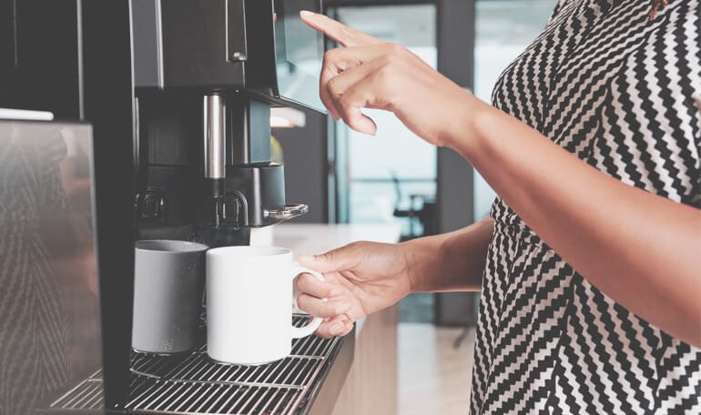 Person laver en kop kaffe ved kaffemaskinen