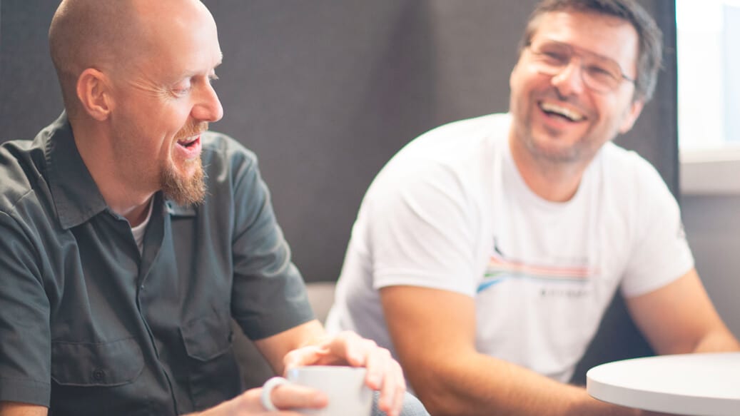 To mandlige kolleger taler og griner på arbejdspladsen