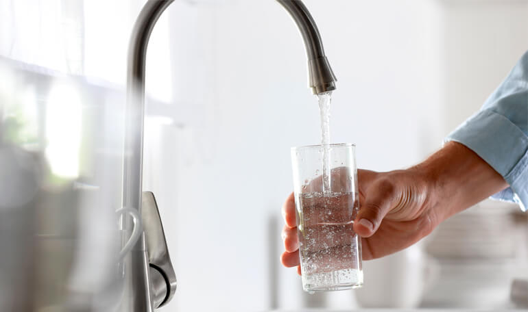 Person fylder glas med vand under vandhane