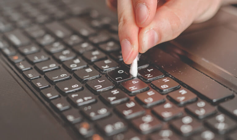 Person rengør tastatur med vatpind