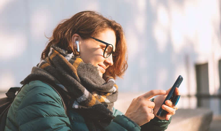 Person udenfor med air pods i ørerne trykker på smartphoneskærm