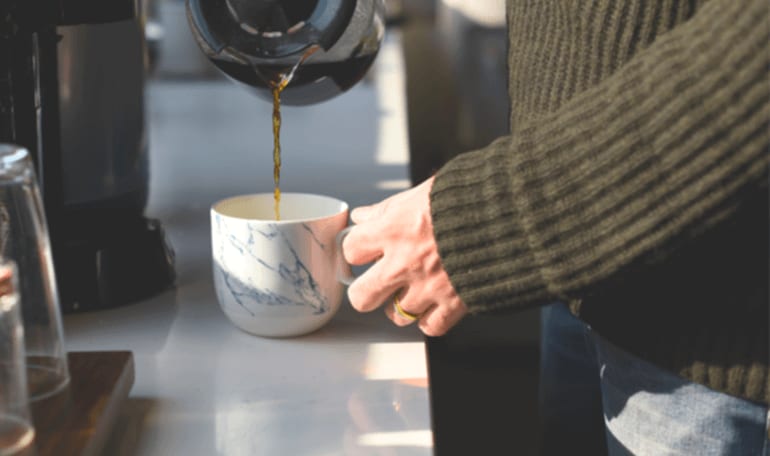 Person hælder kaffe i kop fra kaffekande